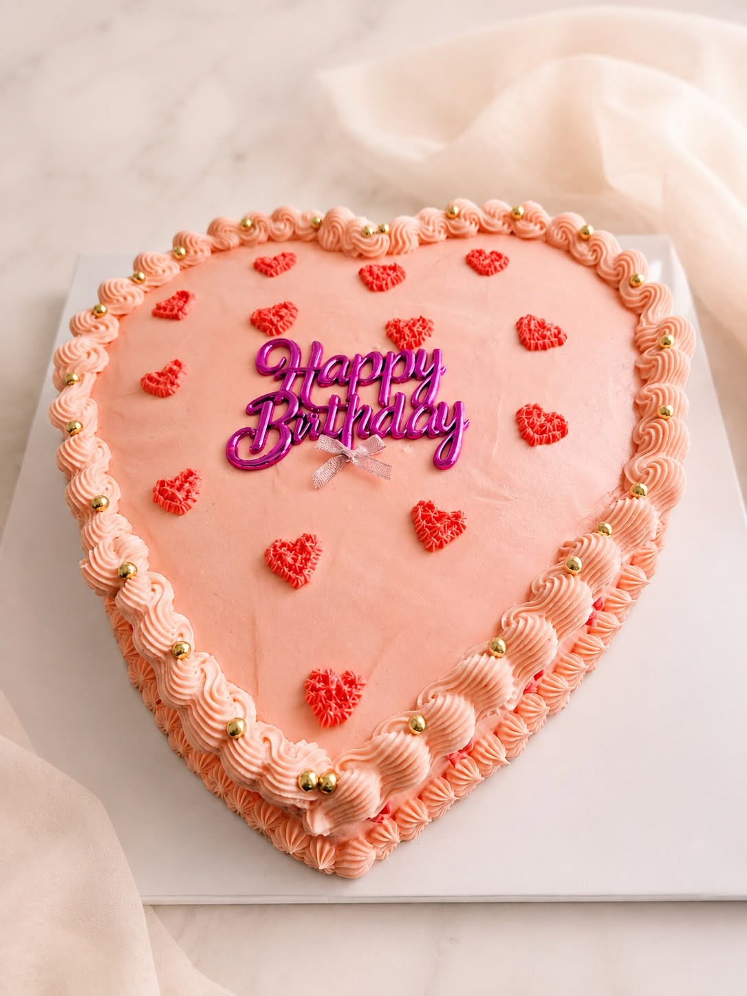 Pink heart-shaped birthday cake with piped borders and small red hearts